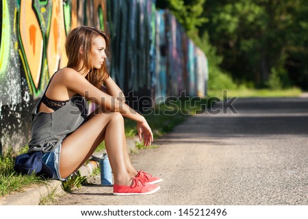 Young Girl Sitting Near A Wall With Graffiti. Outdoors