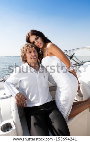 Fashion lovely beautiful couple posing on the boat in open sea in summer. Young man and sensual brunette outdoor portrait in classic dress near the ocean. Outdoors, lifestyle.