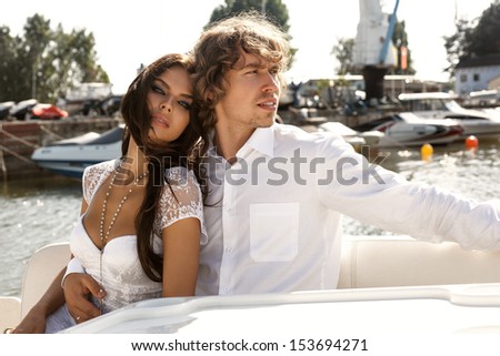 Fashion lovely beautiful couple posing on the luxury boat in open sea in summer. Young man and sensual brunette outdoor portrait in classic dress near the ocean. Outdoors, lifestyle.