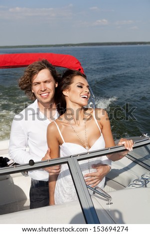 Fashion lovely beautiful couple posing on the luxury boat in open sea in summer. Young man and sensual brunette outdoor portrait in classic dress near the ocean. Outdoors.