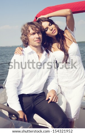 Fashion lovely sensual couple posing on the luxury boat in open sea in summer. Young man and sensual brunette outdoor portrait in classic dress. Outdoors, lifestyle.