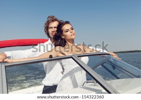 Sexy couple enjoying on the luxury boat in open sea in summer. Young man and sensual brunette outdoor portrait in classic dress. Outdoors, lifestyle.
