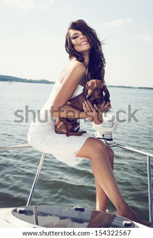 happy beautiful woman with dog on the luxury boat in open sea in summer. Caucasian female model. Outdoors, lifestyle.