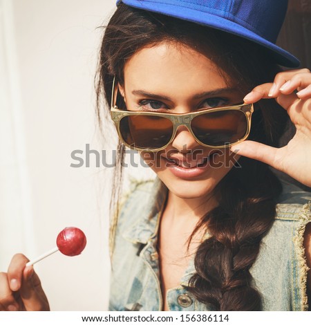Young sexy woman in blue cap and jeans jacket  looking at camera  through sunglasses .  Outdoors, lifestyle.