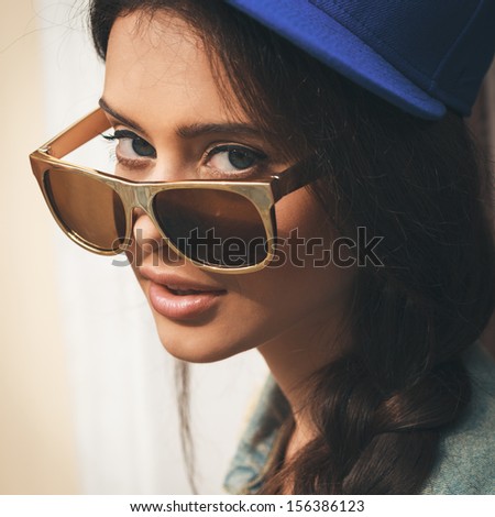 Closeup of Young sexy woman in blue cap and jeans jacket  looking through golden sunglasses .  Outdoors, lifestyle.