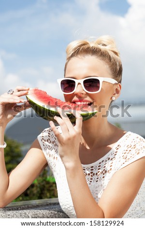 Pretty woman takes watermelon from the opened fridge full of vegetables and fruit. Concept of healthy and dieting food
