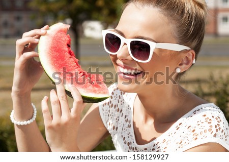 Young smiling woman takes watermelon from the opened fridge full of vegetables and fruit. Concept of healthy and dieting food