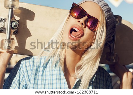 A happy woman playing the ape on the street and holding skateboard behind her head. The girl in joyful feelings. Outdoors, lifestyle.