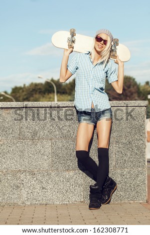A young woman playing the ape on the street and holding skateboard behind her head. The girl in joyful feelings. Outdoors, lifestyle.