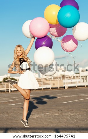 Happy young pretty woman having fun with colorful latex balloons. Gorgeous thick wavy hair. Outdoors, lifestyle