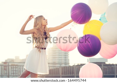Sensual young woman big colorful latex balloons against the evening sun going down. Pastel colors. Outdoors, lifestyle