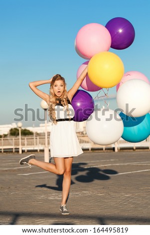 Trendy young woman having fun with big colorful latex balloons.  Gorgeous thick wavy hair. Outdoors, lifestyle