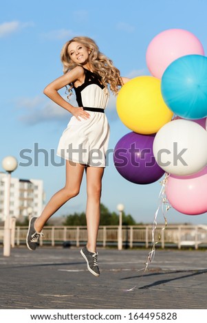 Happy young woman flying with big colorful latex balloons.  Gorgeous thick wavy hair. Outdoors, lifestyle