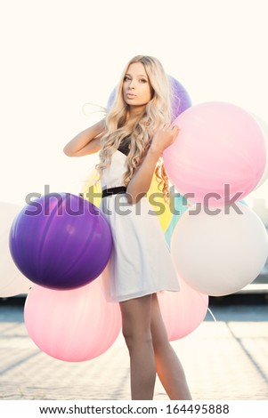 Happy young woman with big colorful latex balloons against the evening sun going down. Outdoors, lifestyle