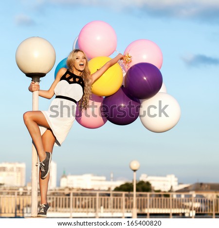Happy young blond  woman with big colorful latex balloons. Beauty Romantic Girl Outdoors. Woman having fun on a lamppost on the background of blue sky.