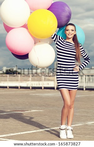 Happy young beautiful woman with colorful latex balloons looking at camera. Outdoors, lifestyle