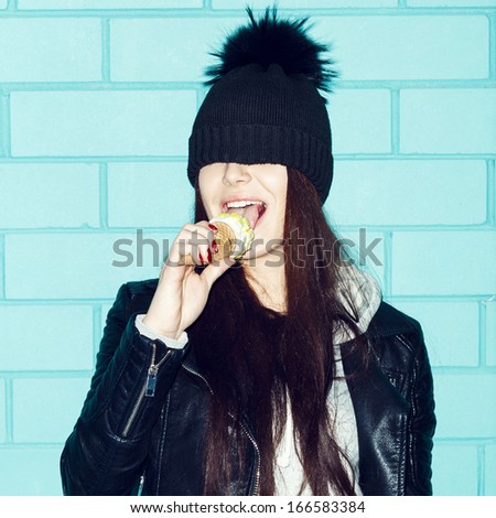 Young Woman In Leather Jacket And Hat Eating Ice Cream Over Blue Brick Wall. Funky Girl Having Fun. Indoors, Lifestyle