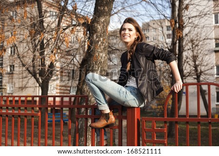 Portrait Of A Beautiful Girl Hipster. Naughty Young Woman Sitting On The Fence. Outdoors, Lifestyle.