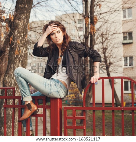 Portrait of a beautiful girl hipster. Trendy naughty woman sitting on the fence. Outdoors, lifestyle.
