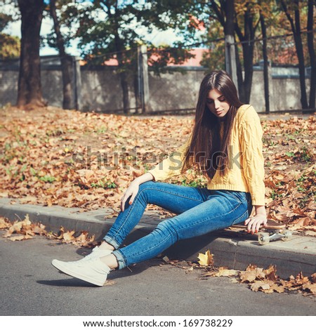 Beautiful young girl sitting on longboard in the afternoon. Skateboarding. Outdoors, lifestyle