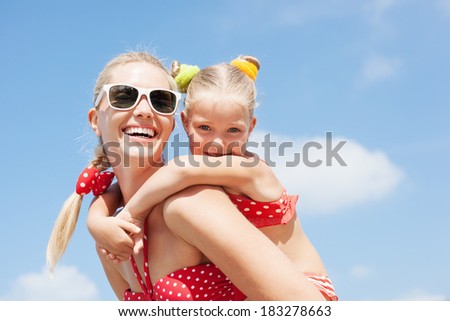Young happy mother with little girl on her back Happy family resting at beach in summer Young happy mother with little girl on her back Happy family resting at beach in summer