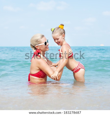 Young happy mother teaching daughter to swim. Happy family resting at beach in summer