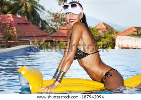 Sexy woman with beauty tanned body sitting on yellow air mattress in the pool in summer and having fun. Outdoor fashion portrait of happy girl in sunglasses