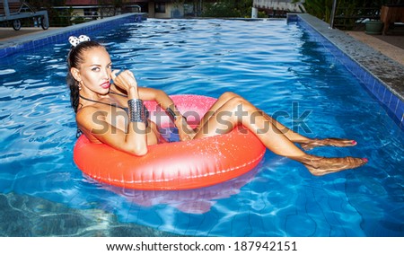 Sexual young woman floating in an inner tube in a swimming pool. Outdoors, lifestyle