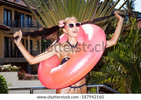Woman in white sunglasses with pink inner tube pulls her hair in different directions for the two arms of the tail . Outdoors