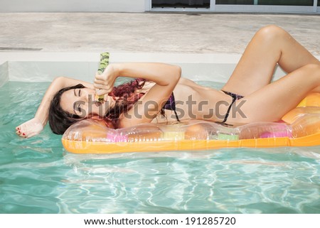 Young woman eating watermelon in swimming pool