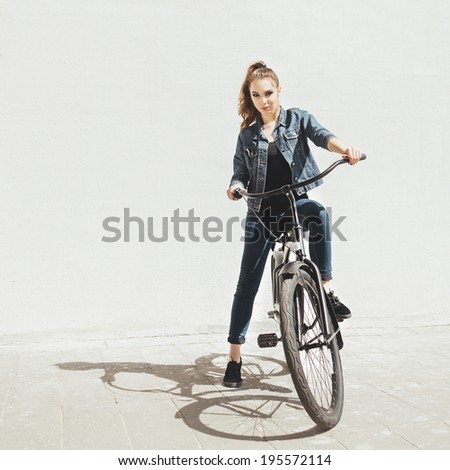 Girl hipster standing with black bike near wall. Outdoor lifestyle portrait