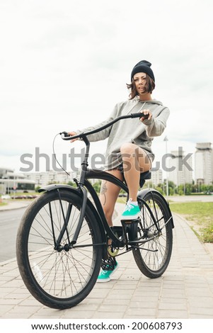 Young hipster girl riding on black bike. Outdoor lifestyle portrait