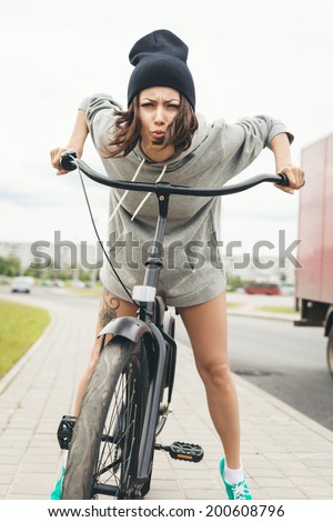 Young hipster girl on black bike making a face at camera. Outdoor lifestyle portrait