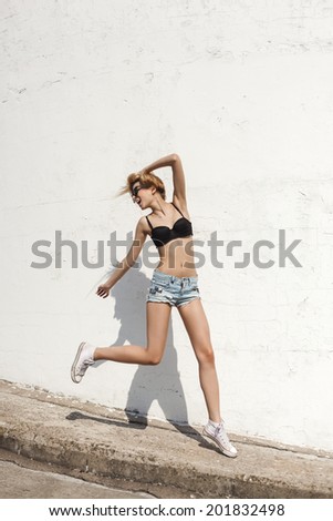 Young sexy woman in sunglasses  posing by the wall and having fun. Outdoor portrait