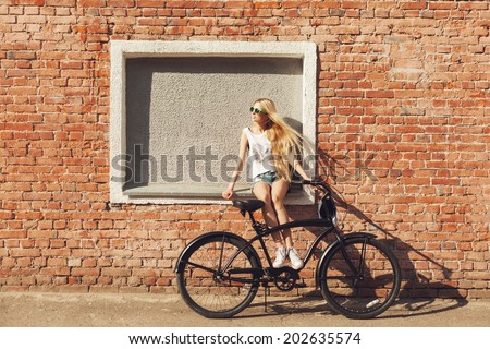Young woman sitting on city bicycle near brick wall. Outdoor lifestyle portrait of girl with cruiser.