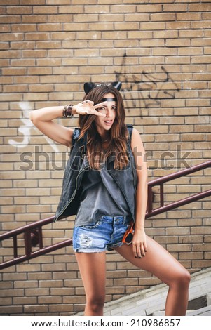 Bad sexy woman with leather cat ears showing fingers and tongue. Urban scene. Outdoor lifestyle portrait