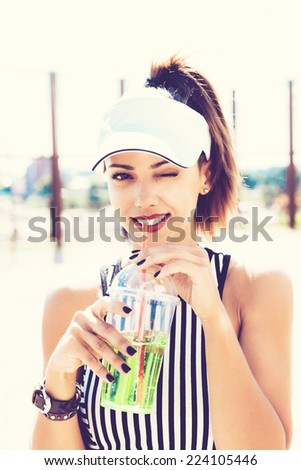 Sporty smiling woman drinking water against the sports ground. Outdoor lifestyle portrait