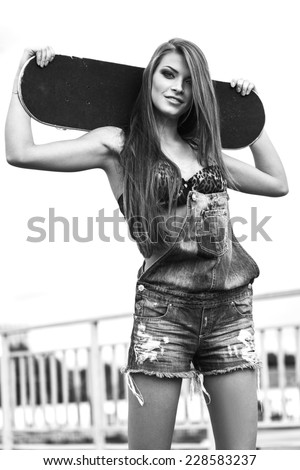 Beautiful Young woman holding a skateboard. Black white portrait of sporty girl