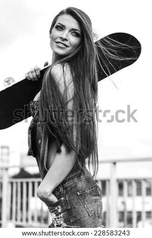 Beautiful Young woman walking and holding a skateboard. Black white portrait of sporty girl