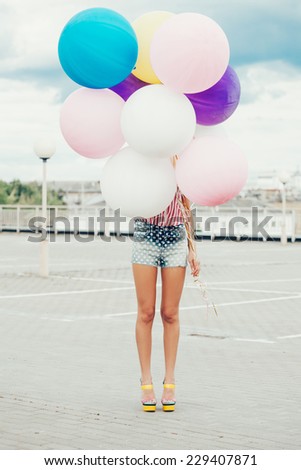Happy young woman standing behind big colorful latex balloons. Outdoors, lifestyle
