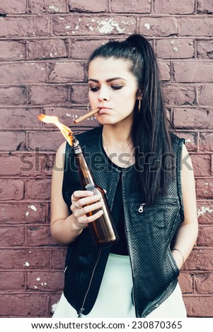 Bad white girl lighting up a cigarette from Molotov cocktail bomb in her hand.  Outdoor lifestyle portrait