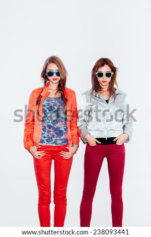 Two young sporty girl friends in sunglasses standing together.  indoor portrait. White background not isolated