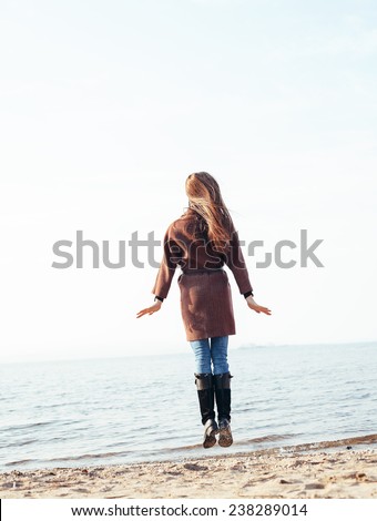 Happy young woman jump on coast on windy day. Outdoor lifestyle portrait