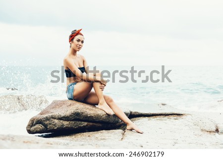 Girl sitting on the rocks on the shore of the sea, contemplating the ocean. Well being healthy lifestyle