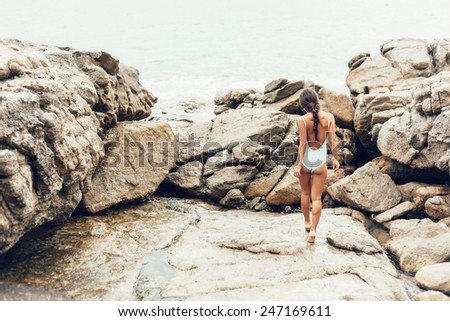 Young woman in a bathing suit walking on rocks by ocean. Well being healthy lifestyle