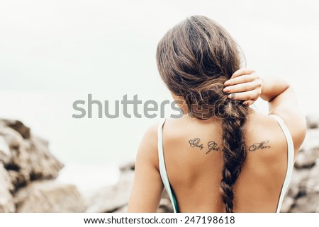 Close-up of back of young woman in a swimsuit standing on the shore and  looking at the sea. Well being healthy lifestyle outdoor