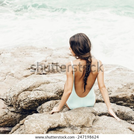 Pretty sexy girl in a swimsuit sitting on the shore and  looking at the sea. Vertical. Well being healthy lifestyle outdoor