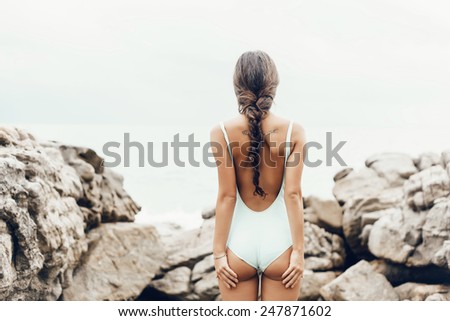 Young woman in a swimsuit standing on the shore and  looking at the sea. Well being healthy lifestyle outdoor