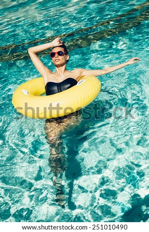 Young pretty fashion woman body posing in summer in pool with clear water lying inner tube and having fun. Well being healthy lifestyle