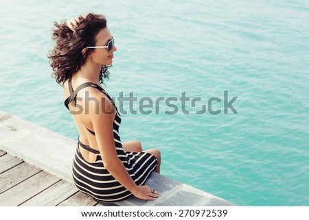Sexy woman sitting alone on the pier near the sea and looking on the water and waiting for somebody in ocean